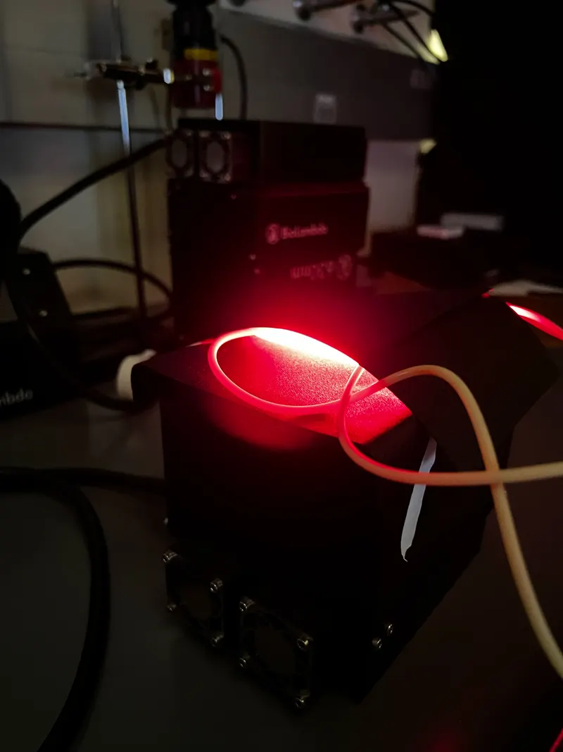 A flexible fiber optic line glowing bright red as it passes through a dark laboratory box.