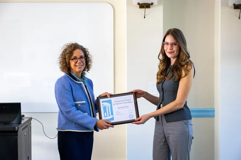 Two women smiling and holding a framed "Postdoctoral Award for Research Excellence" certificate awarded to Marta Overchuk.